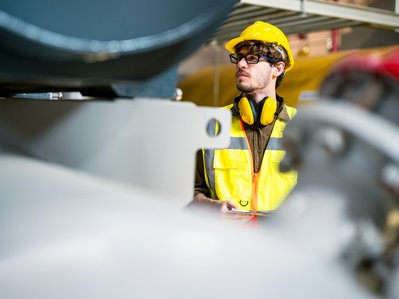 Ingenieur mit Schutzhelm und reflektierender Weste arbeitet in einer Fabrikhalle. Konzentration und Sicherheit stehen im Vordergrund.