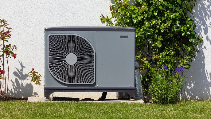 Außen aufgestellte Wärmepumpe neben Hauswand, umgeben von Pflanzen. Stromverbrauch Wärmepumpe im Fokus für energieeffizientes Heizen.
