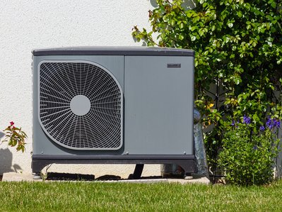 Außen aufgestellte Wärmepumpe neben Hauswand, umgeben von Pflanzen. Stromverbrauch Wärmepumpe im Fokus für energieeffizientes Heizen.