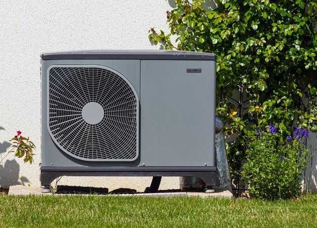 Außen aufgestellte Wärmepumpe neben Hauswand, umgeben von Pflanzen. Stromverbrauch Wärmepumpe im Fokus für energieeffizientes Heizen.