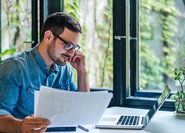 Ein Mann am Schreibtisch prüft Belege an seinem Laptop. Er informiert sich über eine Stromanbieter-Insolvenz.