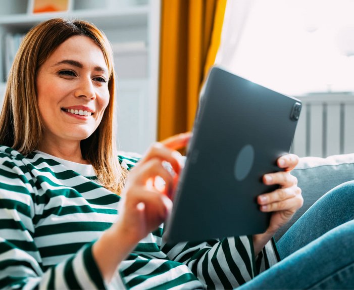 Bild zeigt eine lächelnde Frau mit Tablet auf dem Sofa