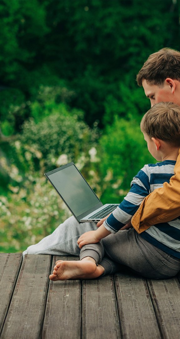 Erwachsener mit Kind auf Holzterrasse, betrachten Laptop. Informationssuche über Umzug und Vertragskündigung bei ENTEGA.