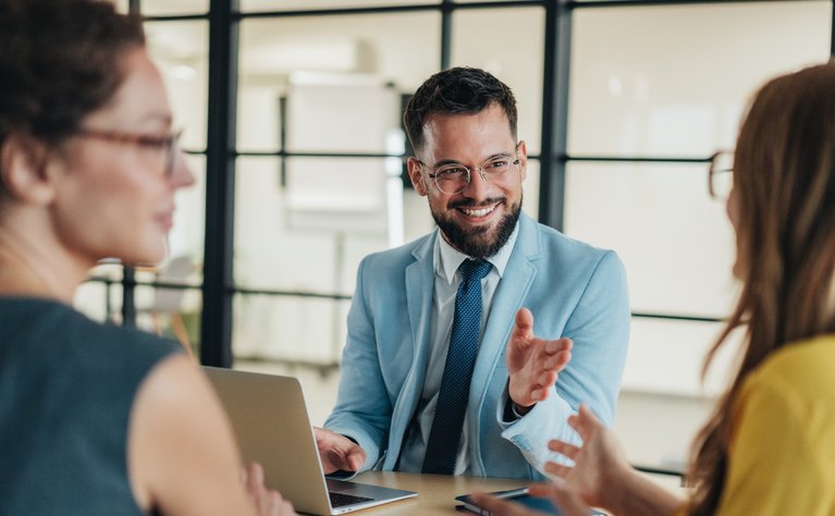 Drei Personen unterhalten sich lebhaft in einem modernen Büro, der Fokus liegt auf integrativer und konstruktiver Zusammenarbeit.