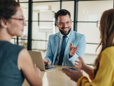 Drei Personen unterhalten sich lebhaft in einem modernen Büro, der Fokus liegt auf integrativer und konstruktiver Zusammenarbeit.