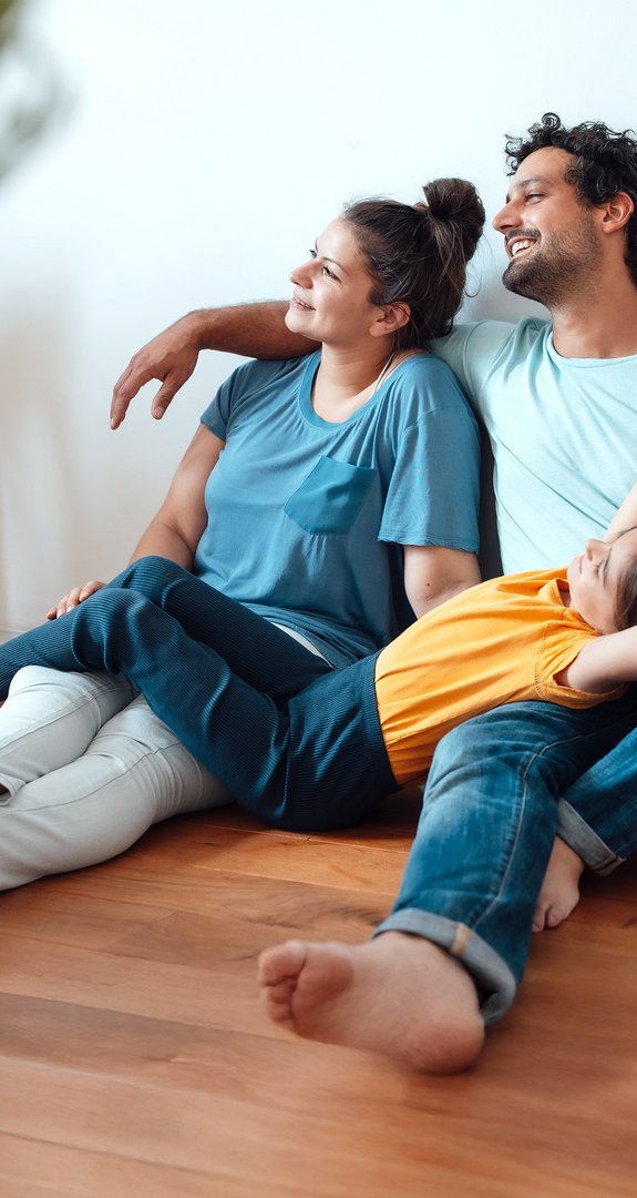 Zufriedene Eltern mit Kind lehnen sich zufrieden an die Wand, stehen für die einfache Verwaltung von ENTEGA Vertragsdetails.