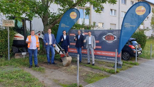 Fünf Personen stehen vor einer Baustelle, heben den Daumen, umgeben von Firmenbannern und ENTEGA Fahnen.