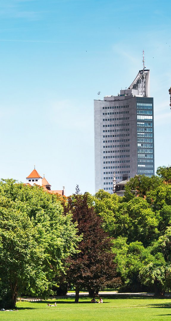 Historischer Turm und modernes Hochhaus hinter Bäumen, Ökostrom Leipzig verbindet Klimaschutz mit Stadtentwicklung.
