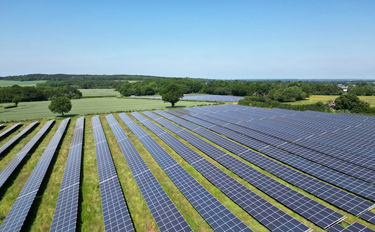 Große Fläche mit Solarmodulen in einem ländlichen Gebiet, fokussiert auf umweltfreundliche und effiziente Stromerzeugung.