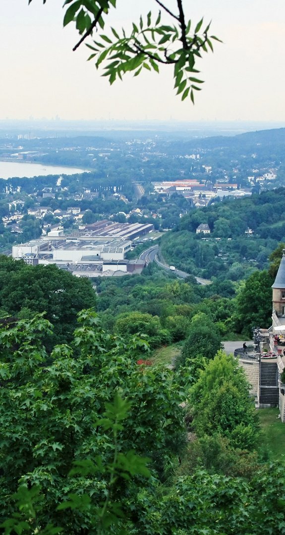 Blick auf Schloss Drachenburg mit Rhein und Bonn im Hintergrund, eingebettet in Natur. Fokus auf Ökostrom Bonn und Umweltbewusstsein.