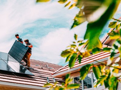 Bild zeigt zwei Installateure beim Installieren von Solarmodulen auf einem Hausdach. 