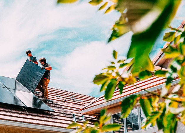 Bild zeigt zwei Installateure beim Installieren von Solarmodulen auf einem Hausdach. 