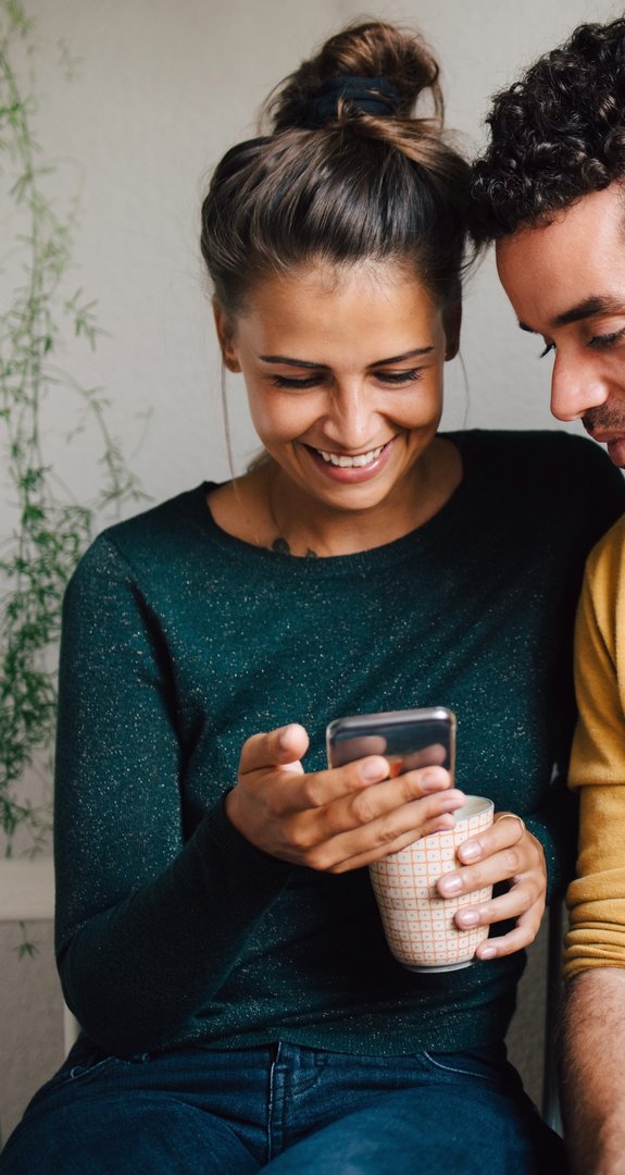 Zwei Freunde sitzen zusammen und freuen sich über die Einlösung einer Empfehlungsprämie auf dem Smartphone.