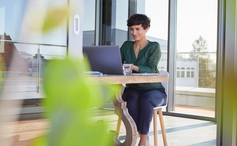 Person arbeitet lächelnd am Laptop in modernem Büro, symbolisiert schnellen Glasfaserzugang für Unternehmen durch ENTEGA.