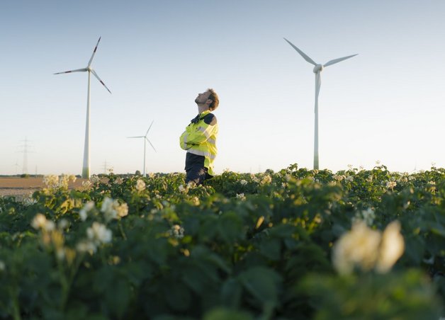 Ein Techniker in Warnjacke prüft Windräder auf Feld. Erneuerbare Energie steht für eine stabile Stromversorgung Deutschland.