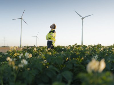 Ein Techniker in Warnjacke prüft Windräder auf Feld. Erneuerbare Energie steht für eine stabile Stromversorgung Deutschland.