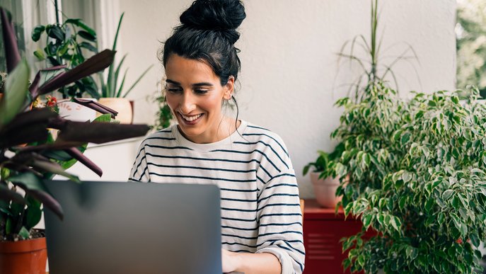 Lächelnde Frau an Laptop in gemütlichem, pflanzenreichem Raum, symbolisiert einfache Übermittlung des Zählerstands und Anpassung des Abschlags.
