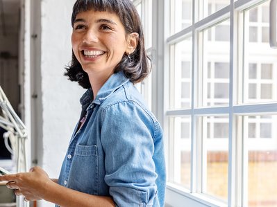 Lächelnde Frau hält Smartphone am Fenster, symbolisiert die einfache Nutzung des ENTEGA Service für Zählerstände und Umzüge.