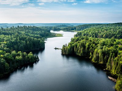 Sanfte Hügel und dichter Wald umgeben einen ruhigen Fluss, hervorgehoben durch klares, sonniges Wetter, zeigt unberührte Natur.