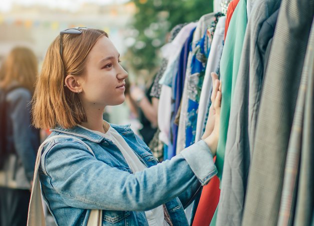 Junge Frau betrachtet Kleidung auf einem Markt, Beusster Konsum im Fokus, nachhaltige Auswahl und Secondhand-Shopping im Freien.