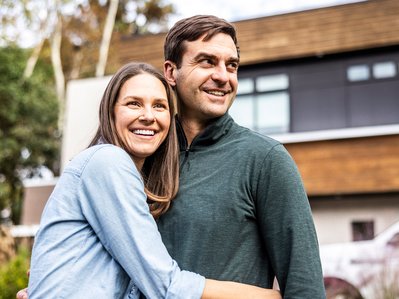 Glückliches Paar vor neuem Haus, Kosten sparen Umzug, Freude über günstigen Wohnungswechsel.