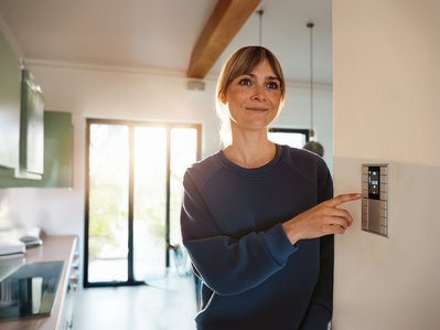 Frau lächelt und passt Thermostat an. Symbolisiert Kosteneinsparung und Energieeffizienz durch gute Heizungsberatung.