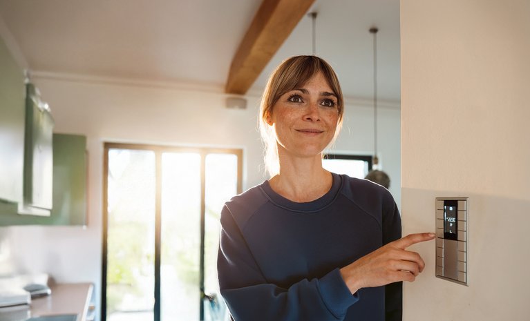 Frau lächelt und passt Thermostat an. Symbolisiert Kosteneinsparung und Energieeffizienz durch gute Heizungsberatung.