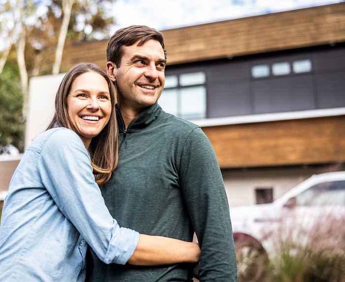 Paar umarmt sich lächelnd im Vorgarten eines modernen Hauses. Steht für Zufriedenheit mit dem Glasfaseranschluss von ENTEGA.