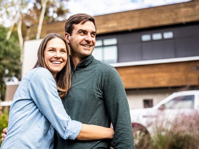 Paar umarmt sich lächelnd im Vorgarten eines modernen Hauses. Steht für Zufriedenheit mit dem Glasfaseranschluss von ENTEGA.