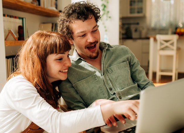Zwei Personen vergleichen am Laptop Daten zum Stromverbrauch 2 Personen Haushalt, moderne Wohnung, bewusster Umgang mit Energie.