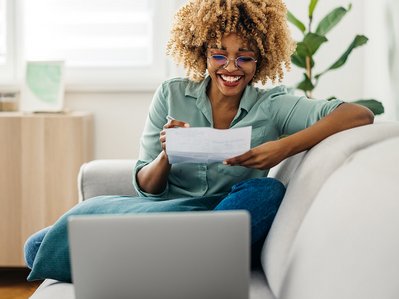 Frau prüft Stromabschlag im Wohnzimmer, Laptop auf dem Schoß; Stromabschlag als zentrales Thema für Haushaltsbudget.