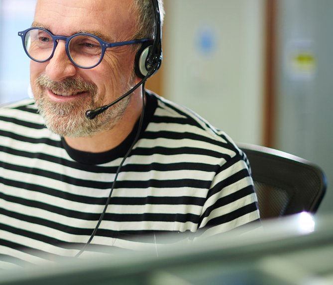 Ein Mann mit Headset in berät freundlich am Telefon, sitzt vor einem Computer in einem Büro.