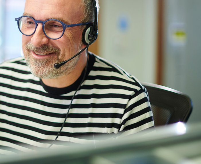Ein Mann mit Headset in berät freundlich am Telefon, sitzt vor einem Computer in einem Büro.