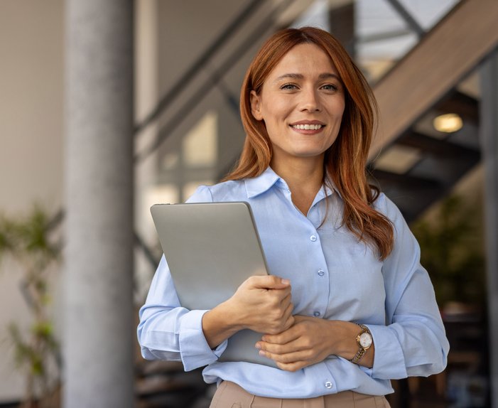 Geschäftsfrau in blauer Bluse steht vor einer stilvollen Bürokulisse. Steht für Angebote von ENTEGA für die Wohnungswirtschaft wie z.B. Ökoenergie oder Gebäudetechnik.