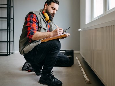 Handwerker prüft Heizung im Neubau und notiert die Kosten für Heizung Neubau auf einem Klemmbrett.