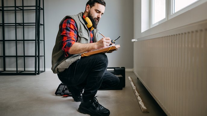 Handwerker prüft Heizung im Neubau und notiert die Kosten für Heizung Neubau auf einem Klemmbrett.