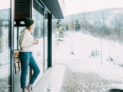 Bild zeigt eine Frau in der Tür ihres Zuhauses in winterlicher Landschaft als Symbolbild für das Heizen mit einer Wärmepumpe