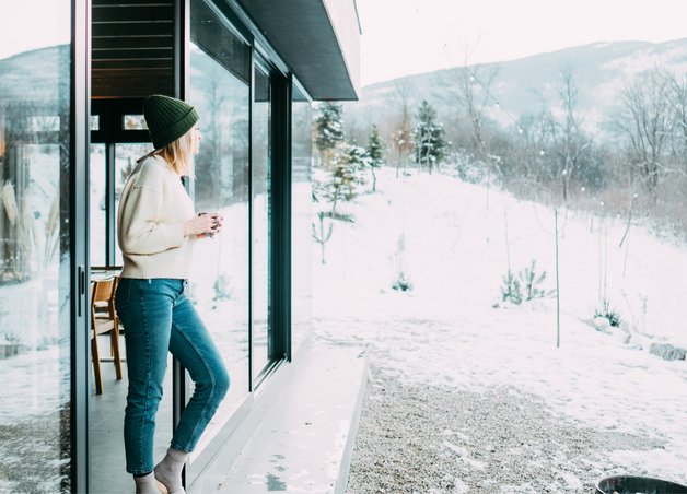 Bild zeigt eine Frau in der Tür ihres Zuhauses in winterlicher Landschaft als Symbolbild für das Heizen mit einer Wärmepumpe