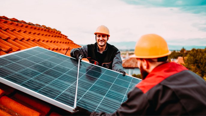 Bild zeigt zwei Bauarbeiter, die Solarmodule auf einem Hausdach installieren