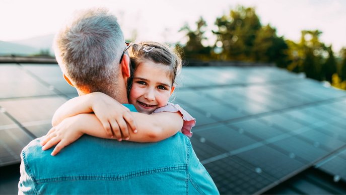 Bild zum Thema PV-Anlage finanzieren: Ein Vater mit Tochter auf dem Arm betrachtet eine installierte Solaranlage
