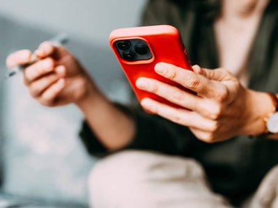 Bild zeigt eine Person mit Stift in der Hand, die auf ihr Smartphone schaut