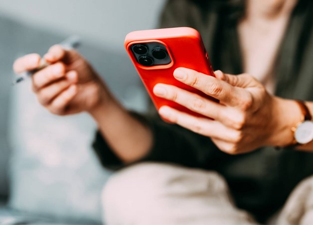 Bild zeigt eine Person mit Stift in der Hand, die auf ihr Smartphone schaut