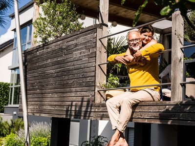 Mann und Kind lachen auf Terrasse, umgeben von Pflanzen. Symbolisiert sorgenfreie Zeit durch zuverlässige Heizungswartung.