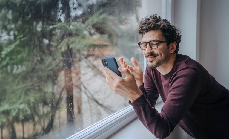 Person schaut in Smartphone, lehnt an regnerischem Fenster. Steht für nachhaltigen Mobilfunk von ENTEGA mit Fokus auf Klima und Komfort.