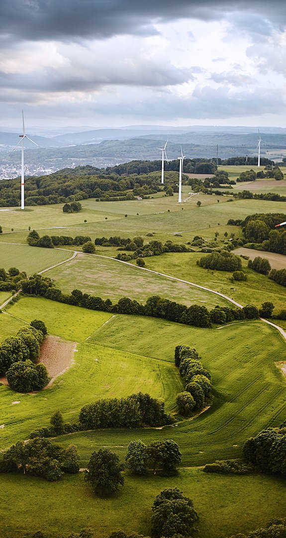 Mehrere Windkraftanlagen auf grünen Feldern unter bewölktem Himmel, repräsentieren erneuerbare Energie.