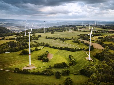 Mehrere Windkraftanlagen auf grünen Feldern unter bewölktem Himmel, repräsentieren erneuerbare Energie.