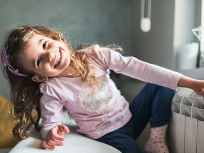 Bild zeigt ein lächelndes Mädchen auf der Couch – moderne Wärmepumpen sorgen dank hohem Wirkungsgrad effizient für wohlige Wärme.