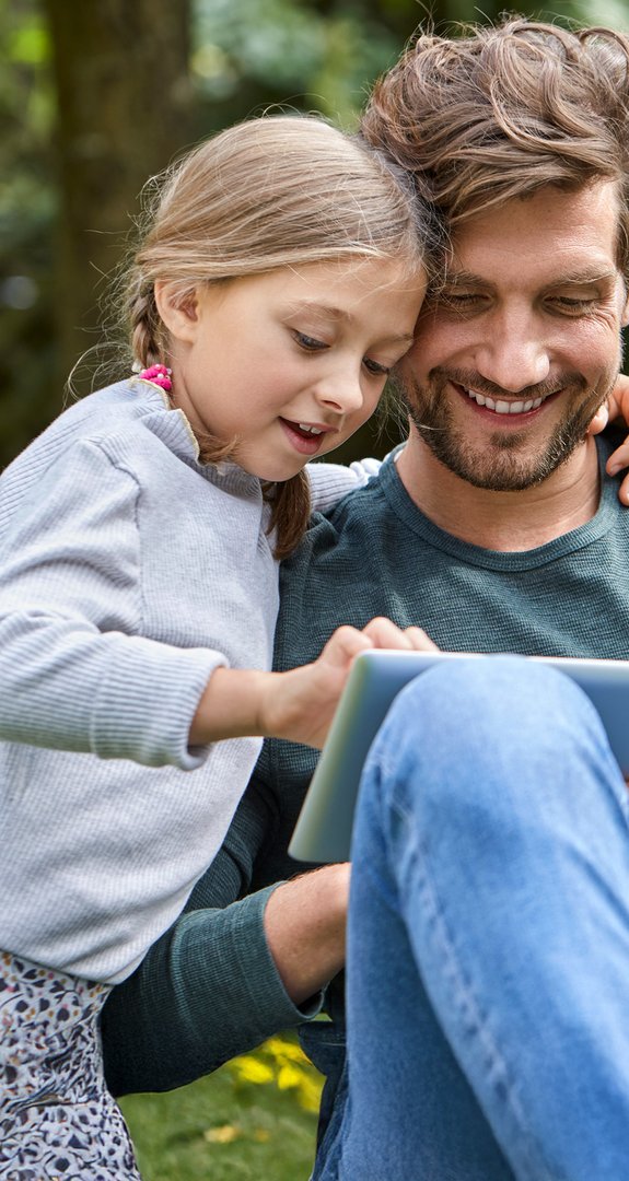 Vater und Tochter sitzen im Garten, betrachten gemeinsam ein Tablet