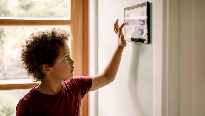 Kind tippt auf Smart-Home-Panel zur Steuerung von Stromverbrauch Licht in heller, moderner Wohnung.