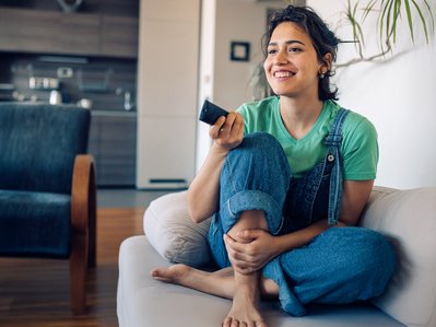 "Lächelnde Person mit Fernbedienung, sitzt zufrieden auf Sofa, symbolisiert entspanntes Fernsehen über ENTEGA TV. "